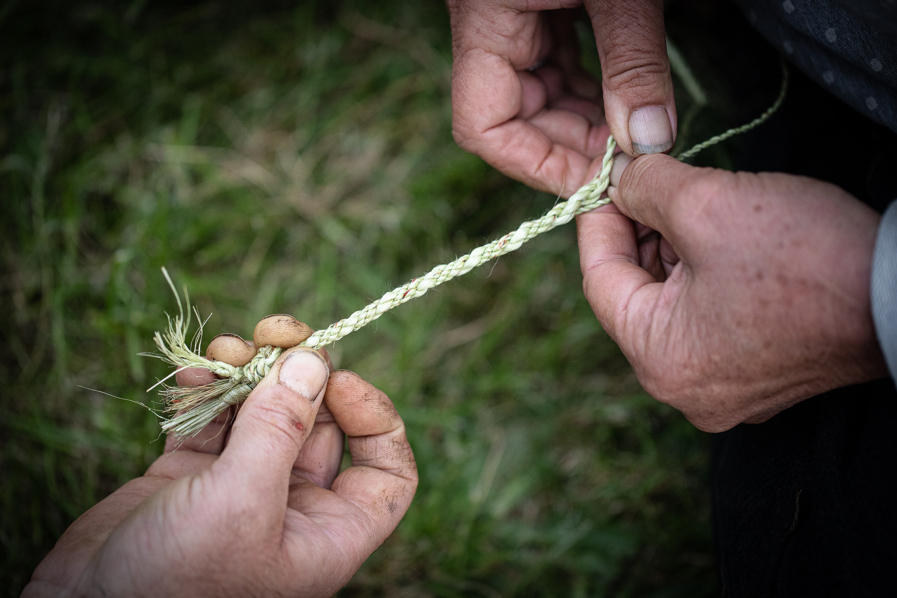 A hand holding flax being weaved with dirty hands 